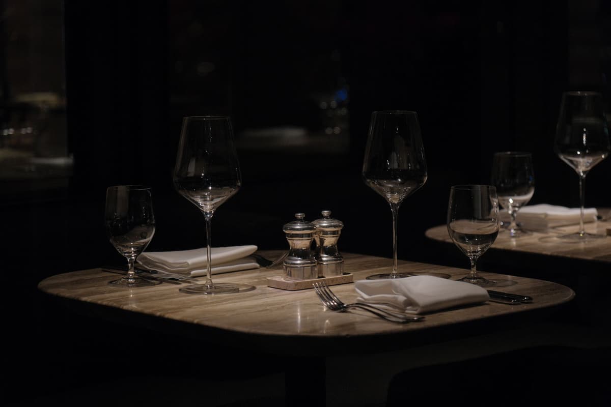 Mesas puestas con copas y servilletas en un salón en penumbra
