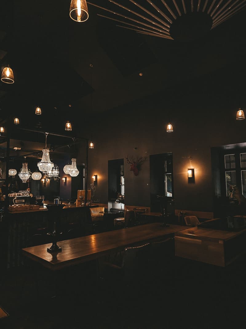 Salón del restaurante en penumbra con lámparas encendidas y mesas de madera