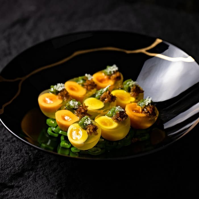 Tomates amarillos sobre quelites en un plato negro con borde dorado