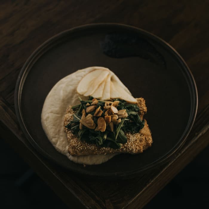 Tostada con quelites salteados y nuez sobre crema, en plato oscuro