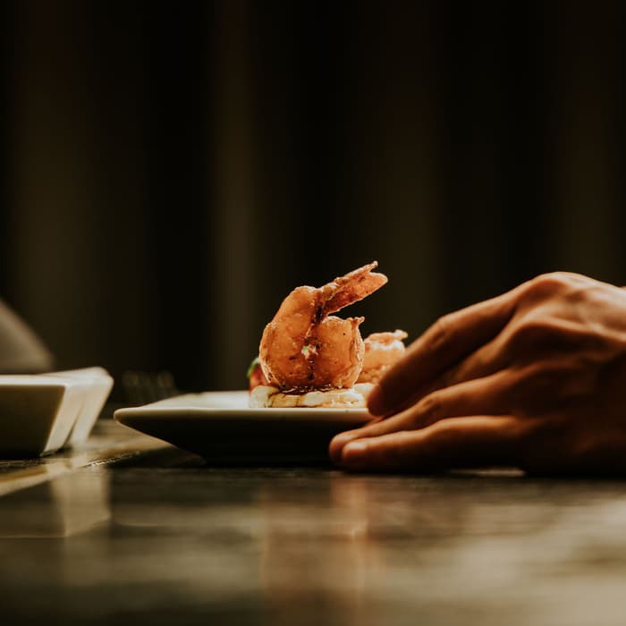 Mano colocando en la barra un plato con camarón a la leña