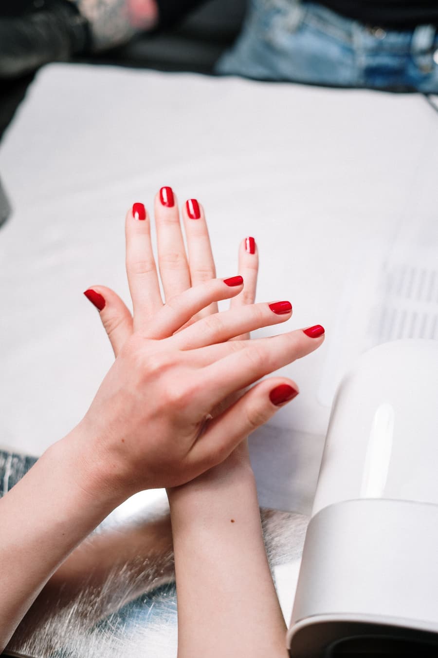 Dos manos con manicure rojo cereza sobre una mesa blanca del estudio