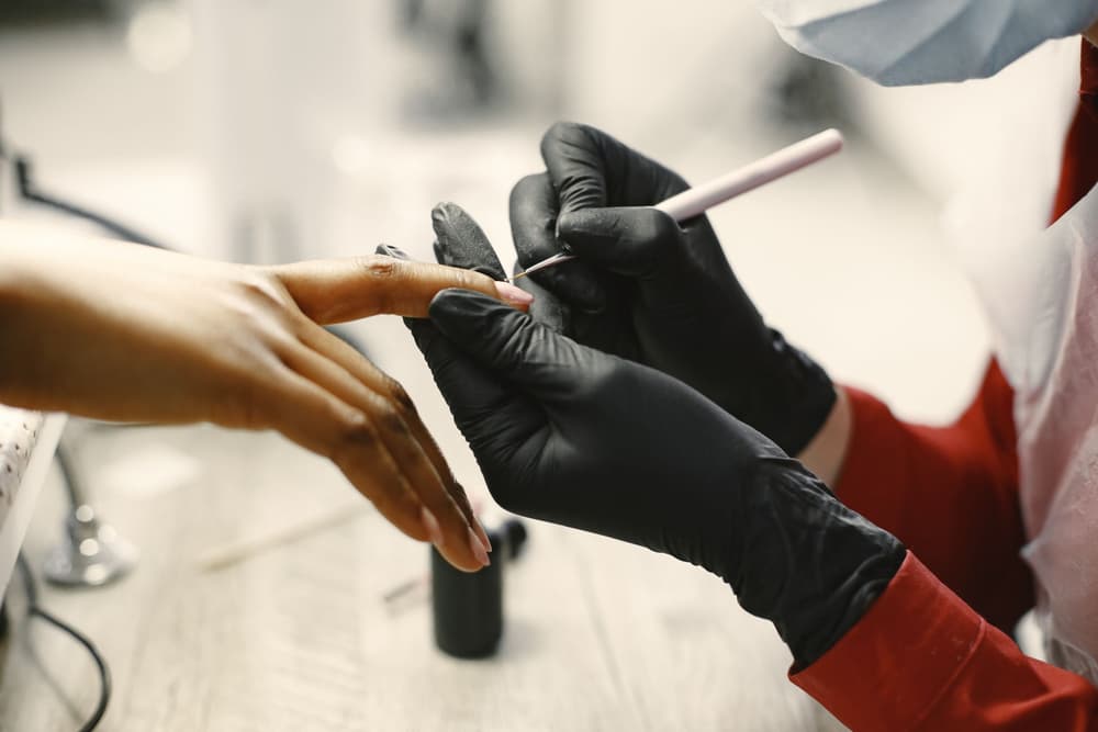 Técnica con guantes negros aplicando esmalte en el estudio