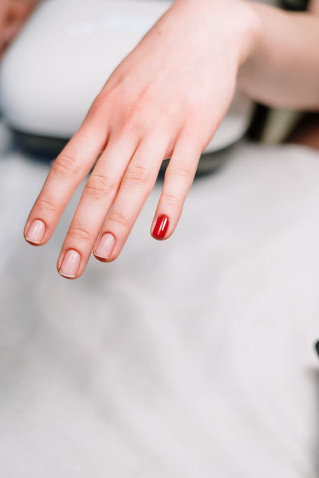 Mano con una uña pintada de rojo durante el servicio