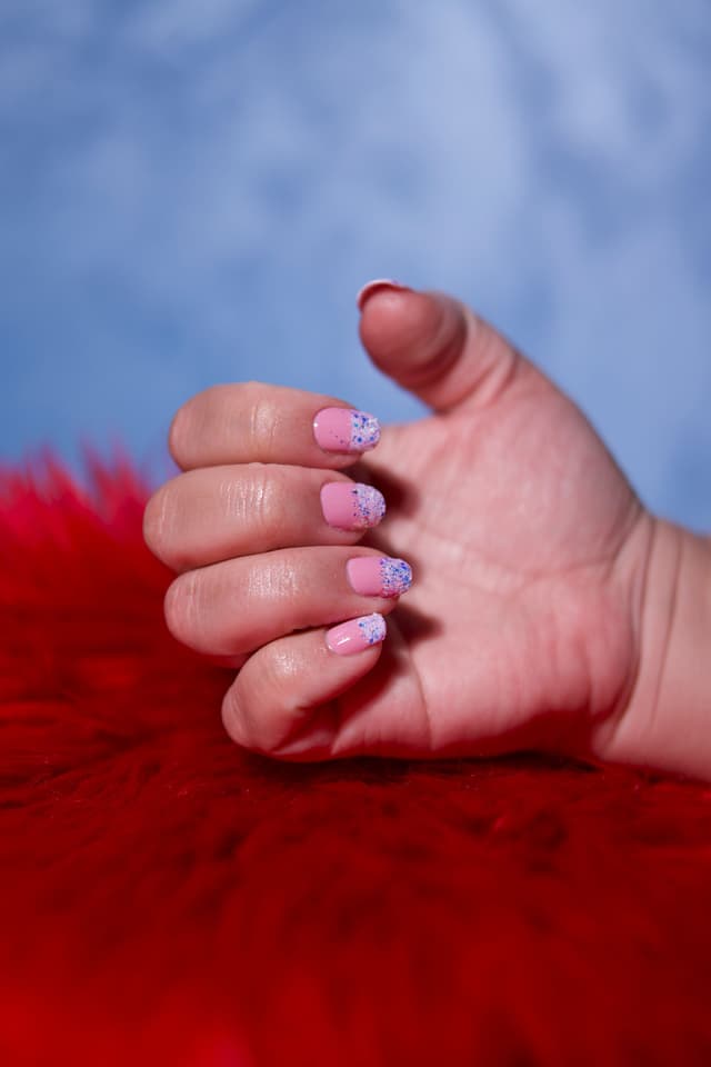 Uñas rosas con glitter sobre fondo rojo