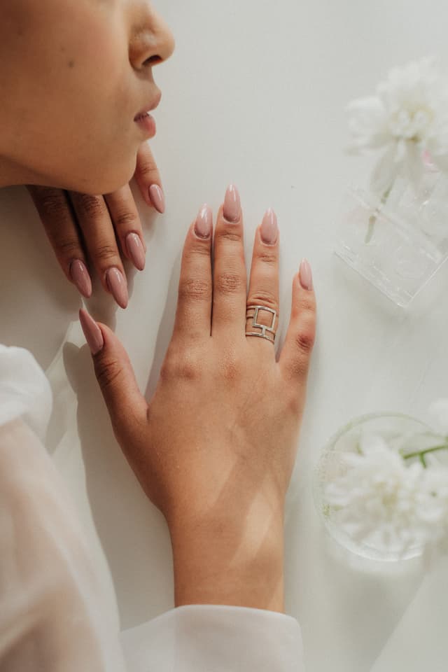 Mano con uñas nude en forma almendra junto a flores blancas