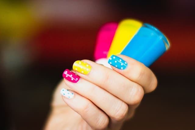 Uñas de colores con puntos sosteniendo frascos de esmalte