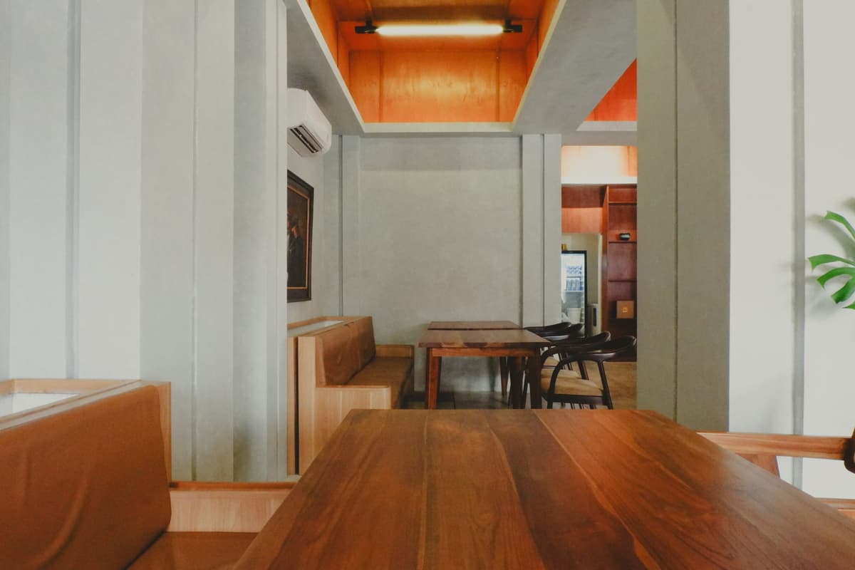 Salón de café con mesa larga de madera, muros claros y luz natural