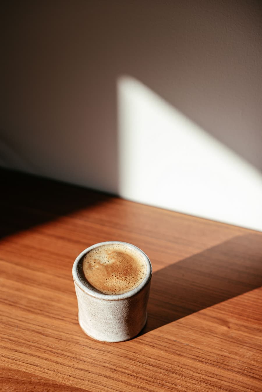 Taza de café con leche sobre una mesa de madera iluminada por un rayo de sol