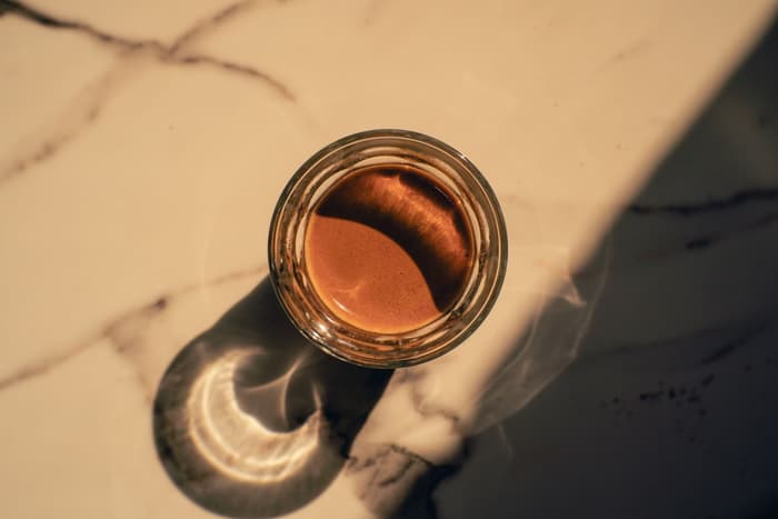 Vista cenital de un espresso en vaso sobre mármol, con su sombra proyectada por el sol