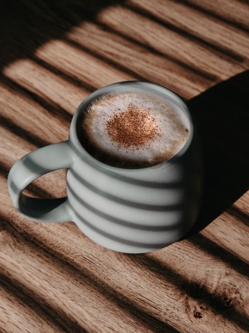 Taza de café recién servida sobre madera, con franjas de sol