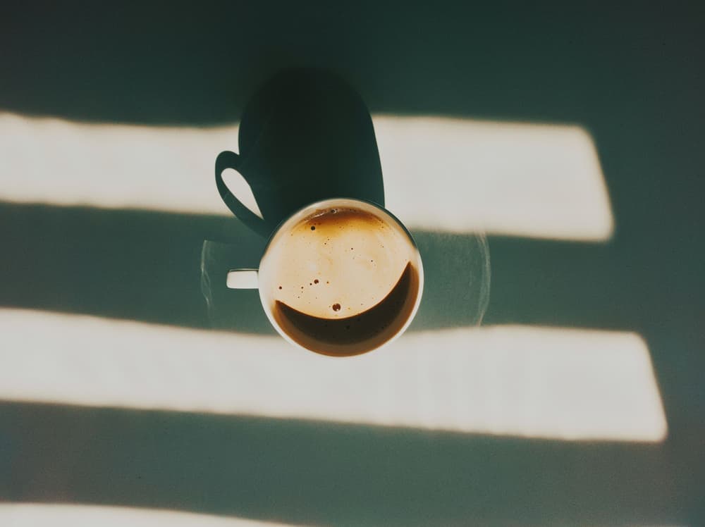 Vista cenital de una taza de café sobre un fondo verde oliva atravesado por franjas de luz